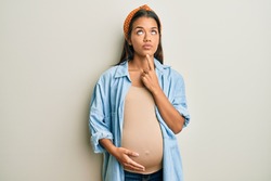 Beautiful hispanic woman expecting a baby, touching pregnant belly thinking concentrated about doubt with finger on chin and looking up wondering 
