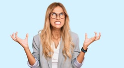 Beautiful blonde young woman wearing business clothes crazy and mad shouting and yelling with aggressive expression and arms raised. frustration concept. 