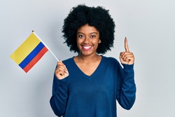 Young african american woman holding colombia flag smiling with an idea or question pointing finger with happy face, number one 