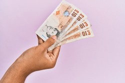 Hispanic hand holding 10 uk pounds banknotes over isolated pink background.