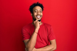 Young african american man with beard wearing casual red t shirt looking confident at the camera with smile with crossed arms and hand raised on chin. thinking positive. 