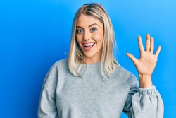 Beautiful blonde woman wearing casual clothes showing and pointing up with fingers number five while smiling confident and happy. 