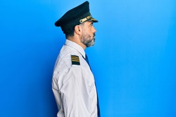 Middle age man with beard and grey hair wearing airplane pilot uniform looking to side, relax profile pose with natural face with confident smile. 