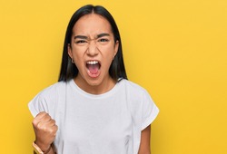 Young asian woman wearing casual white t shirt angry and mad raising fist frustrated and furious while shouting with anger. rage and aggressive concept. 