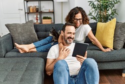 Middle age hispanic couple smiling happy and using touchpad. Sitting on the sofa with dogs at home.