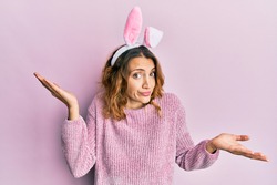 Young caucasian woman wearing cute easter bunny ears clueless and confused with open arms, no idea and doubtful face. 