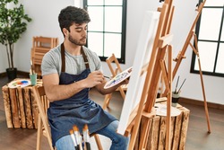 Young hispanic artist man concentrated painting at art studio