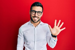 Young hispanic businessman wearing shirt and glasses showing and pointing up with fingers number five while smiling confident and happy. 