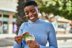 Young african american woman smiling happy counting south africa rand banknotes at the city.