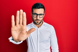 Young hispanic businessman wearing shirt and glasses doing stop sing with palm of the hand. warning expression with negative and serious gesture on the face. 