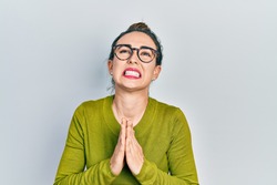 Young hispanic girl wearing casual clothes and glasses begging and praying with hands together with hope expression on face very emotional and worried. begging. 