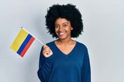 Young african american woman holding colombia flag looking positive and happy standing and smiling with a confident smile showing teeth 