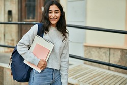 Young middle east student girl smiling happy holding book at the city.