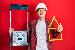 Young hispanic man wearing handyman uniform holding construction stairs and house project smiling and laughing hard out loud because funny crazy joke. 