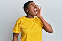 Young african american woman wearing casual yellow t shirt shouting and screaming loud to side with hand on mouth. communication concept. 