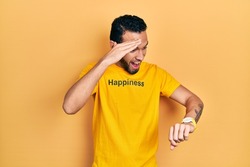Hispanic man with beard wearing t shirt with happiness word message looking at the watch time worried, afraid of getting late 