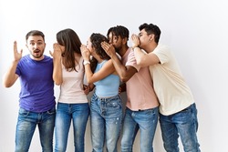 Group of young people standing together over isolated background hand on mouth telling secret rumor, whispering malicious talk conversation 