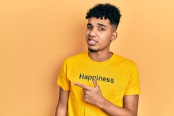 Young african american man wearing t shirt with happiness word message pointing aside worried and nervous with forefinger, concerned and surprised expression 