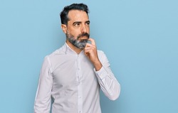 Middle aged man with beard wearing casual white shirt serious face thinking about question with hand on chin, thoughtful about confusing idea 