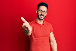 Young hispanic man wearing casual clothes and glasses smiling friendly offering handshake as greeting and welcoming. successful business. 
