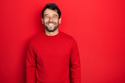 Handsome man with beard wearing casual red sweater with a happy and cool smile on face. lucky person. 