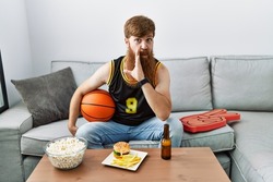 Caucasian man with long beard holding basketball ball cheering tv game hand on mouth telling secret rumor, whispering malicious talk conversation 