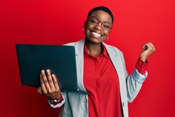 Young african american woman holding laptop screaming proud, celebrating victory and success very excited with raised arm 