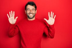 Handsome man with beard wearing casual red sweater showing and pointing up with fingers number ten while smiling confident and happy. 