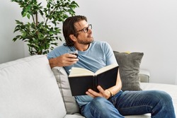 Middle age caucasian man reading book drinking wine at home