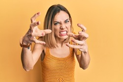Young caucasian blonde woman wearing casual yellow t shirt shouting frustrated with rage, hands trying to strangle, yelling mad 