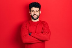 Young arab man with beard wearing casual red sweater happy face smiling with crossed arms looking at the camera. positive person. 