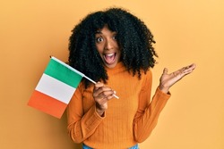 African american woman with afro hair holding ireland flag celebrating achievement with happy smile and winner expression with raised hand 