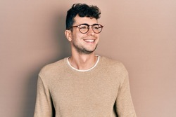 Young hispanic man wearing casual clothes and glasses looking away to side with smile on face, natural expression. laughing confident. 