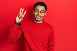 Young african american man wearing casual clothes and glasses showing and pointing up with fingers number three while smiling confident and happy. 