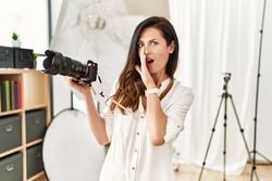 Beautiful caucasian woman working as photographer at photography studio hand on mouth telling secret rumor, whispering malicious talk conversation 