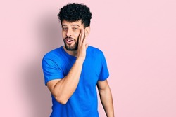 Young arab man with beard wearing casual blue t shirt hand on mouth telling secret rumor, whispering malicious talk conversation 