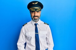 Middle age man with beard and grey hair wearing airplane pilot uniform with a happy and cool smile on face. lucky person. 