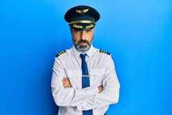 Middle age man with beard and grey hair wearing airplane pilot uniform skeptic and nervous, disapproving expression on face with crossed arms. negative person. 