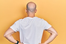 Young bald man wearing casual white t shirt standing backwards looking away with arms on body 