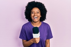 Young african american woman holding reporter microphone smiling and laughing hard out loud because funny crazy joke. 