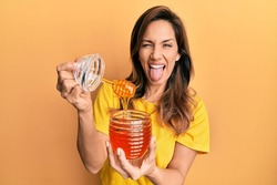 Young latin woman holding honey sticking tongue out happy with funny expression. 