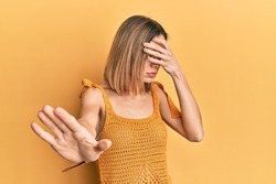 Young caucasian blonde woman wearing casual yellow t shirt covering eyes with hands and doing stop gesture with sad and fear expression. embarrassed and negative concept. 