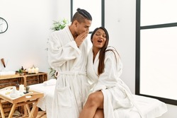 Young latin couple wearing towel standing at beauty center hand on mouth telling secret rumor, whispering malicious talk conversation 
