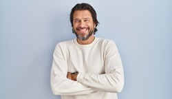 Handsome middle age man wearing casual sweater over blue background happy face smiling with crossed arms looking at the camera. positive person. 