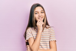 Young brunette girl wearing casual striped t shirt smiling looking confident at the camera with crossed arms and hand on chin. thinking positive. 