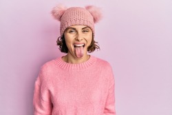 Young brunette woman wearing cute wool cap sticking tongue out happy with funny expression. emotion concept. 