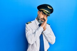 Middle age man with beard and grey hair wearing airplane pilot uniform sleeping tired dreaming and posing with hands together while smiling with closed eyes. 