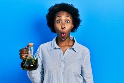 Young african american woman holding olive oil can scared and amazed with open mouth for surprise, disbelief face 