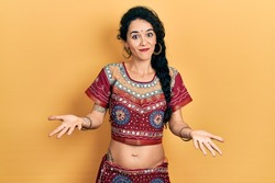 Young woman wearing bindi and bollywood clothing clueless and confused expression with arms and hands raised. doubt concept. 
