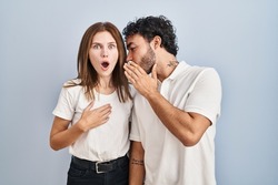 Young couple wearing casual clothes standing together hand on mouth telling secret rumor, whispering malicious talk conversation 
